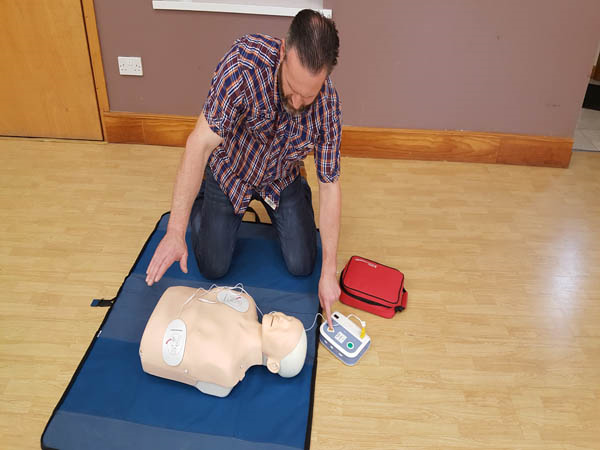 Trainee illustrates how to operate an AED by giving a standby signal